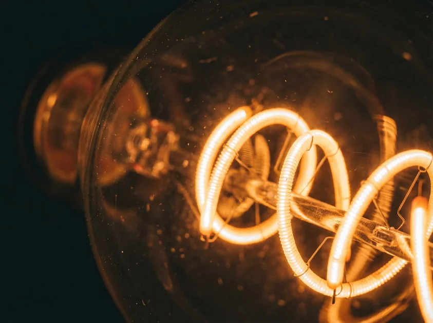 Extreme close-up of Tomalson's curved vintage LED filament, glowing with warm amber light against dark background